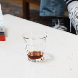 Verse koffiebonen - Bijna leeg glas met wat zwarte koffie op de bodem op een tafel. 