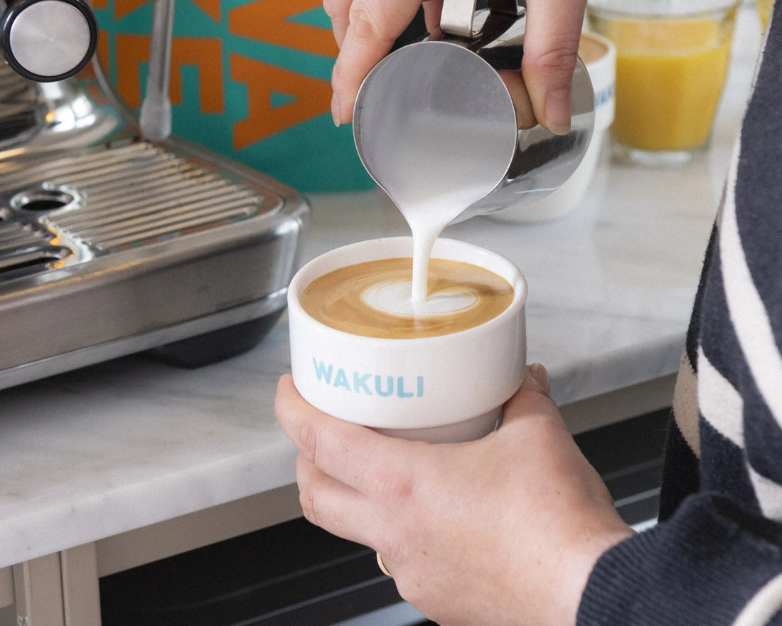 Duurzame koffiecups - Iemand maakt een schuimige cappuccino in een keuken. Espressomachine op de achtergrond.