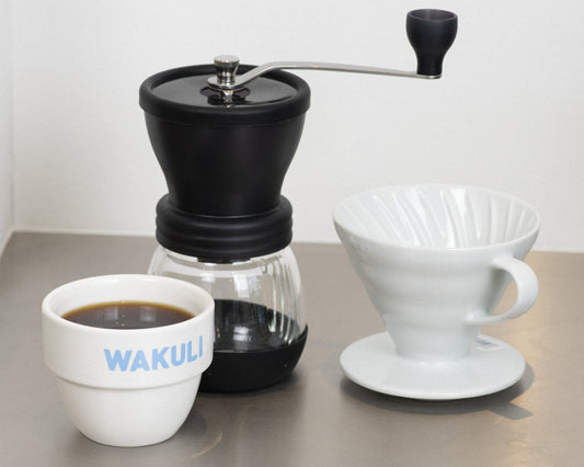 Vers gemalen koffiebonen - Wakuli kopje, koffiemaler en V60 dripper op metal tafel