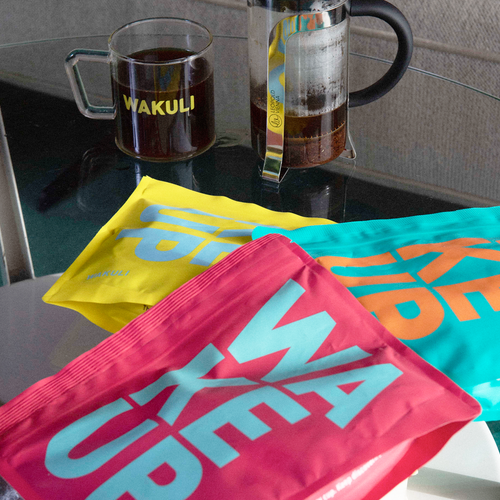 Wakuli koffie proefpakket - Drie Wakuli koffiezakken liggen op elkaar op een tafel. French press koffie op de achtergrond.