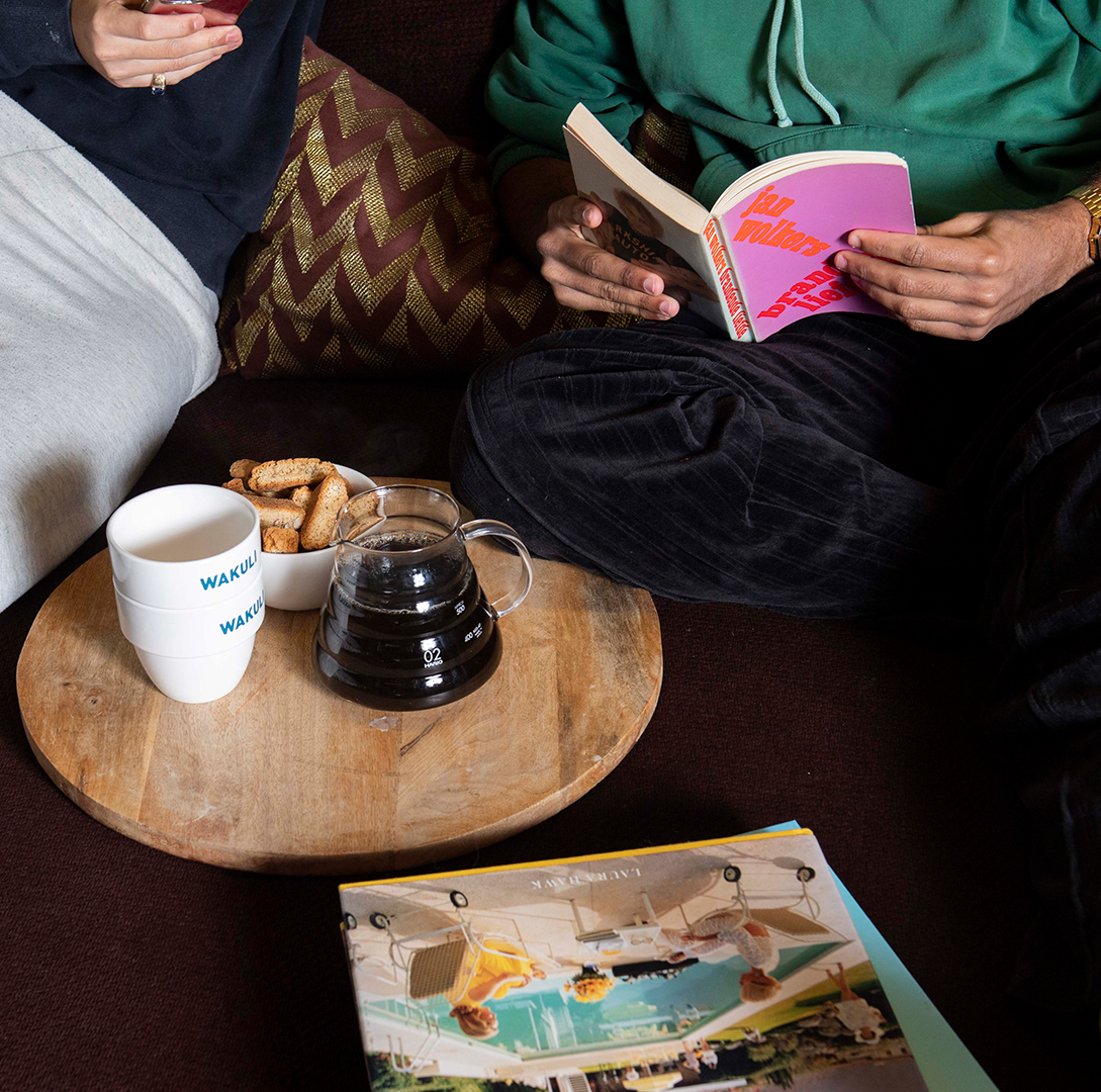 Wakuli koffie proefpakket - Twee jongens zitten op een bank. Een van hen leest een roze boek. Zwarte koffie en Wakuli-kopjes staan voor hen op tafel.