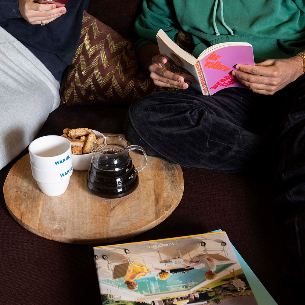 Wakuli koffie proefpakket - Twee jongens zitten op een bank. Een van hen leest een roze boek. Zwarte koffie en Wakuli-kopjes staan voor hen op tafel.