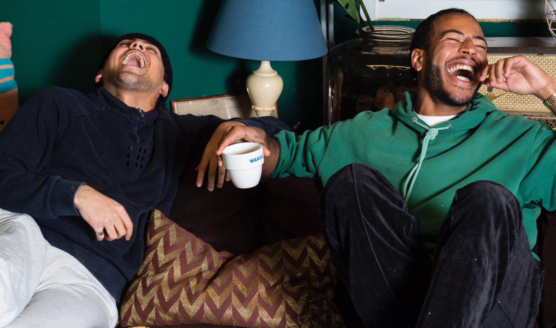 Wakuli koffie - 2 lachende jongens in truien zittend op de bank met Wakuli koffie in hun handen