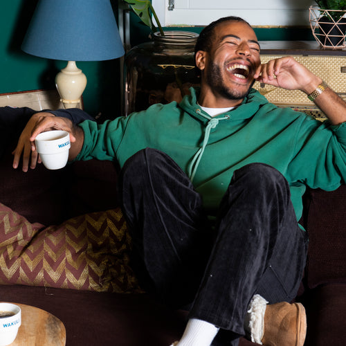 Volautomaat koffie - Jonge man zit op een bruine bank te lachen, terwijl hij een Wakuli koffiebeker in zijn hand houdt.