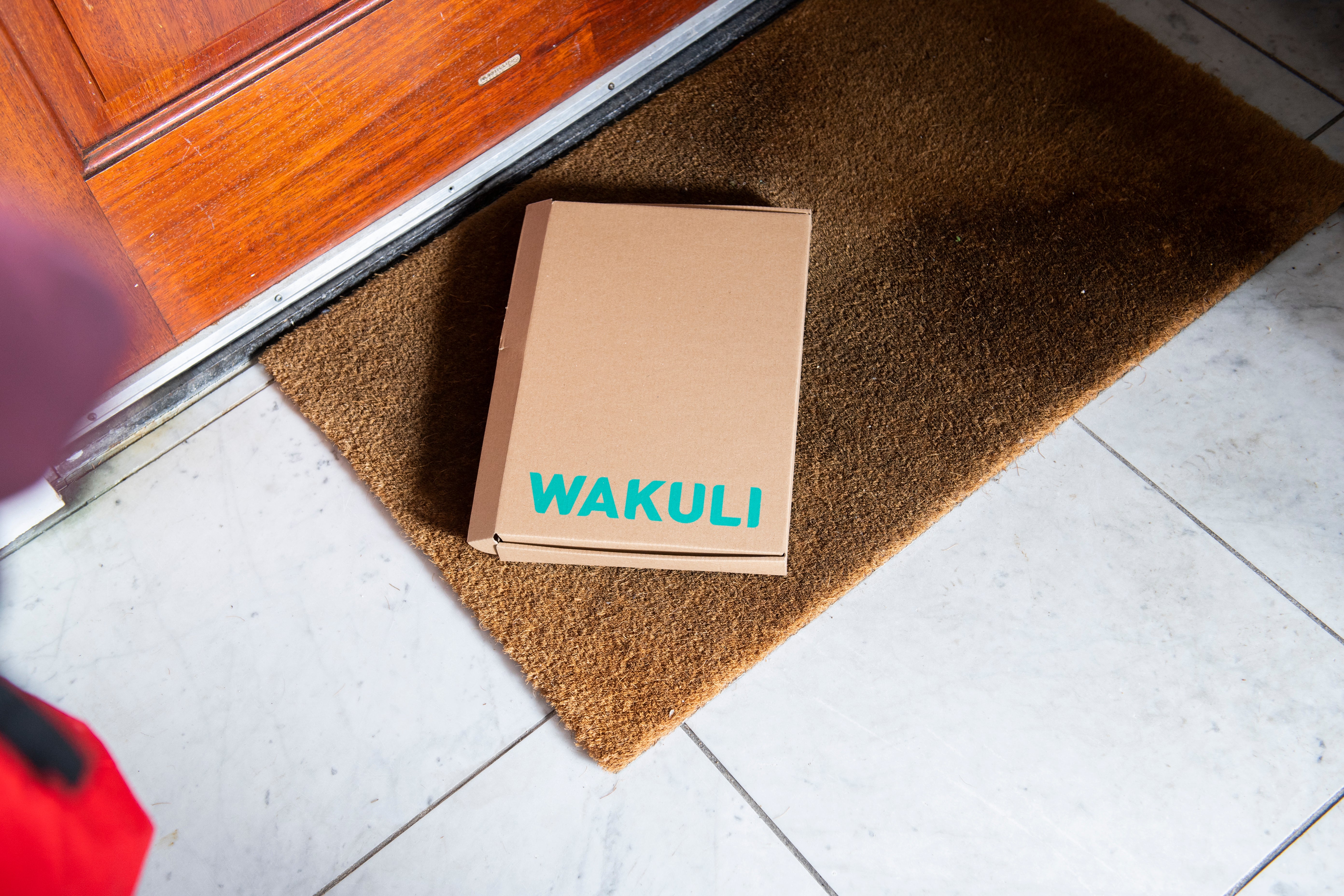 Koffiebonen voor latte - Een kartonnen doos met Wakuli erop ligt op een deurmat voor een bruine deur.
