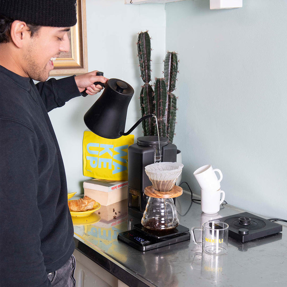 Discover Monthly Light Roast Koffiebonen- Jongen maakt pourover koffie met een V60 in een keuken. Wakuli Discover Monthly en koffiemolen op de achtergrond.
